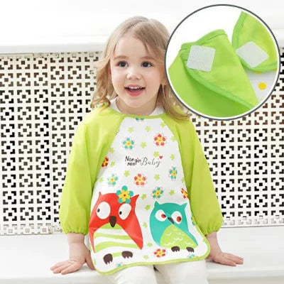 Fille portant un bavoir à manche longue hibou vert, avec un zoom sur la fermeture velcro, soulignant la praticité du bavoir manche longue bébé.