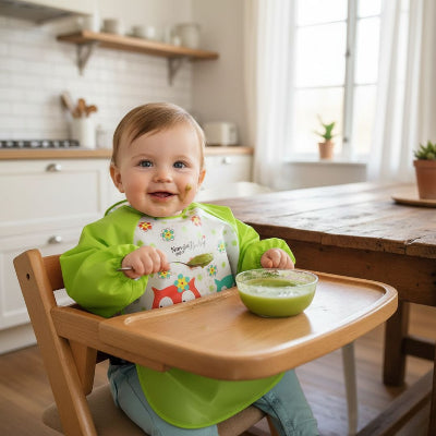 Bébé assis dans une chaise haute portant un bavoir à manche longue vert motif hibou, idéal comme bavoir avec manche bébé imperméable pour protéger les vêtements pendant le repas.