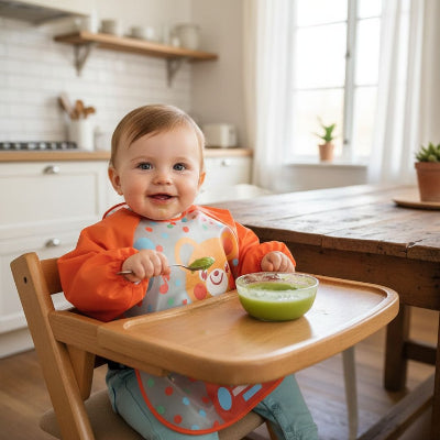 Bébé souriant portant un bavoir à manche longue orange motif ours, parfait comme bavoir à enfiler pour limiter les taches lors de la diversification alimentaire.