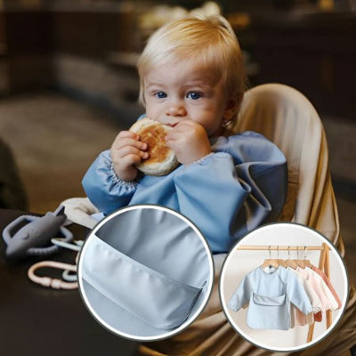 Bébé blond assis en chaise haute portant un bavoir bébé manche longue bleu ciel BabyProtect™, mangeant un petit pain, avec gros plan sur la poche récupératrice.