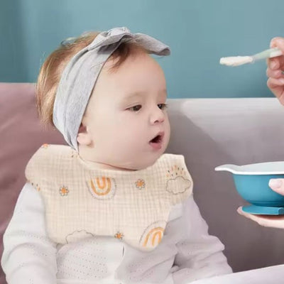 Bébé nourri à la cuillère portant un bavoir bébé manche longue en coton motif arc-en-ciel, bavoir coton repas absorbant et pratique.