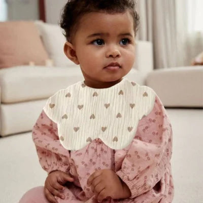 Bébé métisse portant un bavoir bébé manche longue en coton bio motif cœurs, bavoir coton bébé confortable et absorbant pour repas.