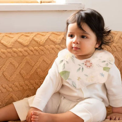 Bébé assis portant un bavoir bébé manche longue en coton avec motif fleurs, bavoir tissu repas doux et respirant.