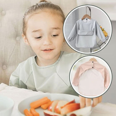Petite fille portant un bavoir bébé manche longue gris clair BabyProtect™, assise à table avec assiette de carottes et pommes, bavoir bébé imperméable pratique.