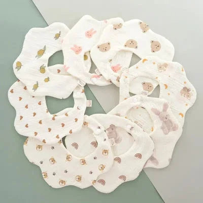 Lot de bavoirs bébé manche longue en coton, motifs variés (lapins, ours, fruits, cœurs, arc-en-ciel) disposés en cercle, bavoir tissu bébé couture.