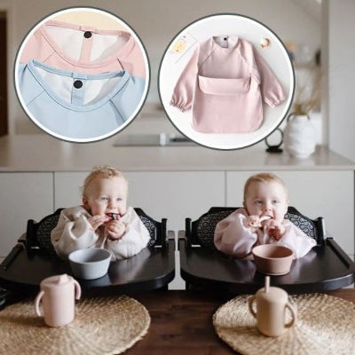 Deux bébés jumeaux assis en chaise haute portant des bavoirs bébé manche longue rose clair BabyProtect™, avec zoom sur la fermeture pression et les détails couture.