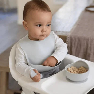 Bébé mange dans une chaise haute avec un bavoir bébé en silicone imperméable avec récupérateur
