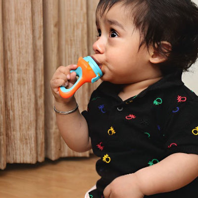 Bébé assis utilisant une grignoteuse bébé orange et bleue pour manger un fruit