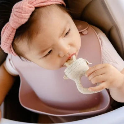 Bébé utilisant une grignoteuse bébé avec un fruit pendant le repas dans sa chaise haute
