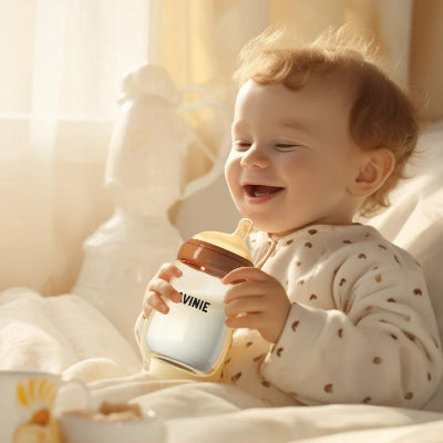Bébé souriant tenant un biberon pour allaitement naturel, transition douce entre sein et biberon.