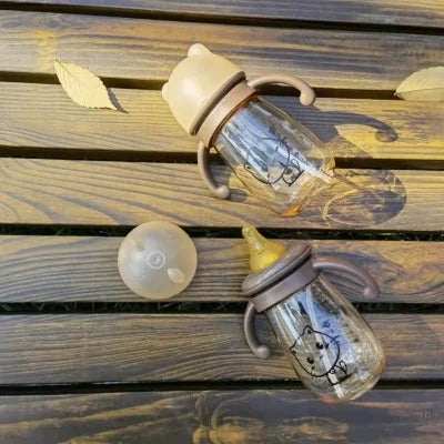Deux biberons en PPSU avec tétine et capuchon oreilles d’ours, posés sur une table en bois, parfaits pour lait maternel ou eau.