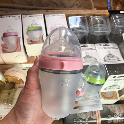 Biberon Como Tomo rose 250 ml en silicone tenu en main devant un stand de produits, parfait pour un allaitement mixte sain et pratique.