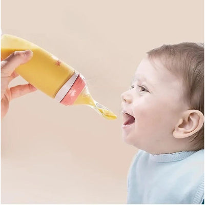 Bébé heureux prêt à déguster une purée avec son biberon cuillère rose ergonomique.