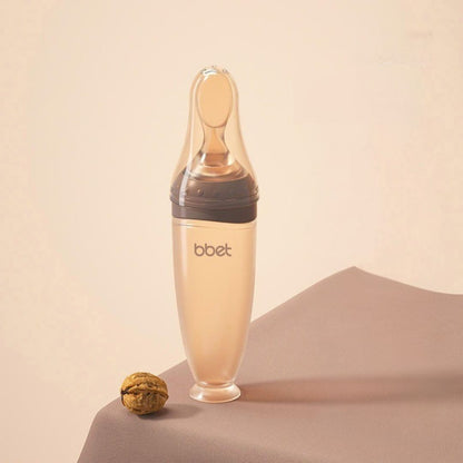 Biberon cuillère en silicone coloris café avec embouts adaptés selon l'âge de bébé, idéal pour les repas en douceur dès 0 mois.
