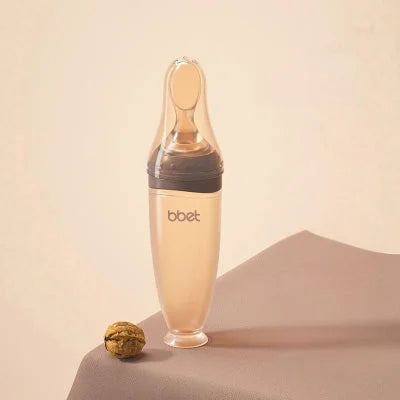 Biberon cuillère en silicone coloris café avec embouts adaptés selon l'âge de bébé, idéal pour les repas en douceur dès 0 mois.
