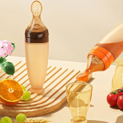 Biberon cuillère orange servant du jus dans un gobelet doseur