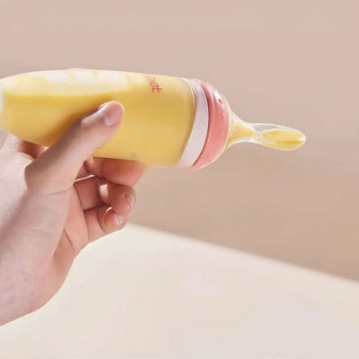 Biberon cuillère rose tenu en main, prêt à nourrir bébé avec une purée douce et onctueuse.