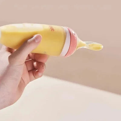 Biberon cuillère rose tenu en main, prêt à nourrir bébé avec une purée douce et onctueuse.