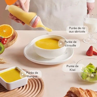 Biberon cuillère rose versant de la purée de fruits dans une assiette de bébé.