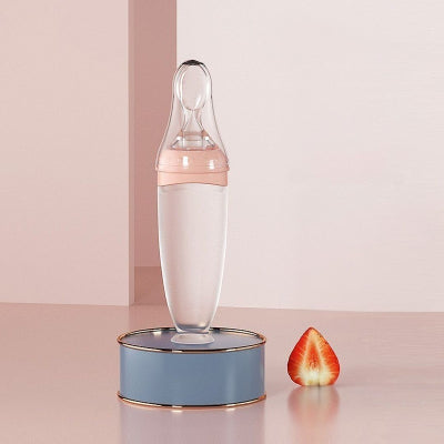 Biberon cuillère rose posé sur un socle bleu avec fraise, ambiance douce et féminine.