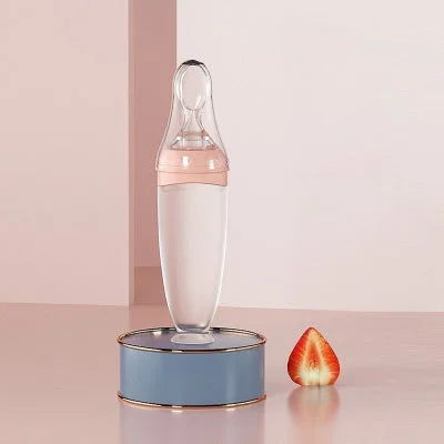 Biberon cuillère rose posé sur un socle bleu avec fraise, ambiance douce et féminine.