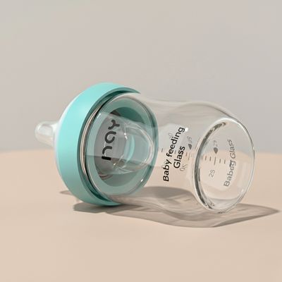 Biberon en verre incassable bleu allongé sur une table beige, design moderne et hygiénique.