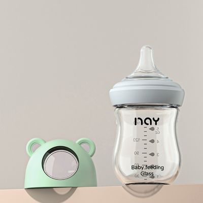 Biberon en verre incassable vert avec capuchon en forme d’ourson, design ergonomique pour bébé allaité.