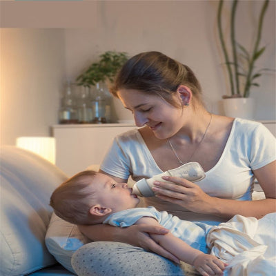 Maman donnant le biberon en verre à son bébé la nuit, pour un moment calme et complice.