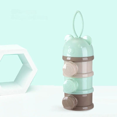 Boite doseuse lait LactoPop™ verte posée sur une surface claire avec fond pastel, équipée d’une anse de transport pratique pour sac ou poussette.