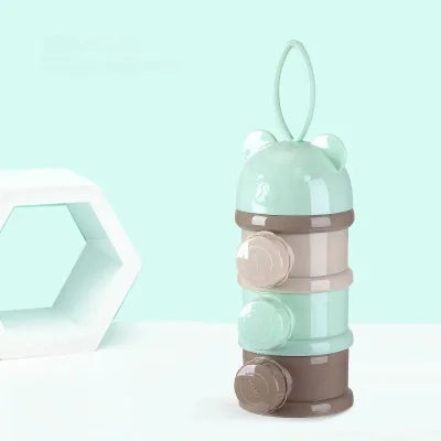 Boite doseuse lait LactoPop™ verte posée sur une surface claire avec fond pastel, équipée d’une anse de transport pratique pour sac ou poussette.
