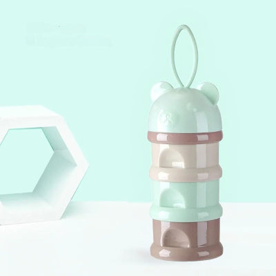  Modèle vert menthe de la boite doseuse lait en forme d’ourson, compartiments empilables sans bouchon visible, sur fond bleu pastel.