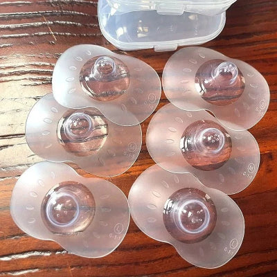 Vue multiple de bouts de seins en silicone souple, posés sur une table en bois, avec boîte rigide en arrière-plan.