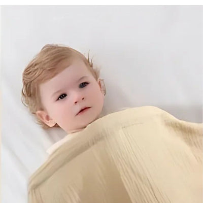 Cape d’allaitement beige utilisée comme couverture pour bébé couché, tissu léger et respirant assurant confort et chaleur douce.

