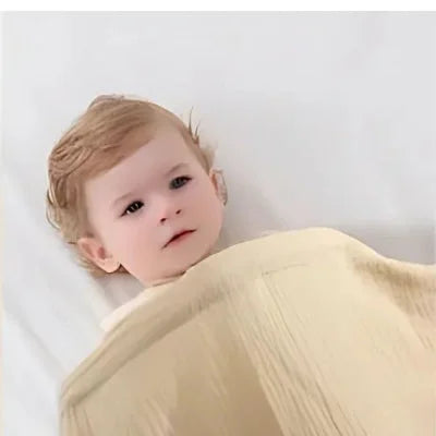 Cape d’allaitement beige utilisée comme couverture pour bébé couché, tissu léger et respirant assurant confort et chaleur douce.

