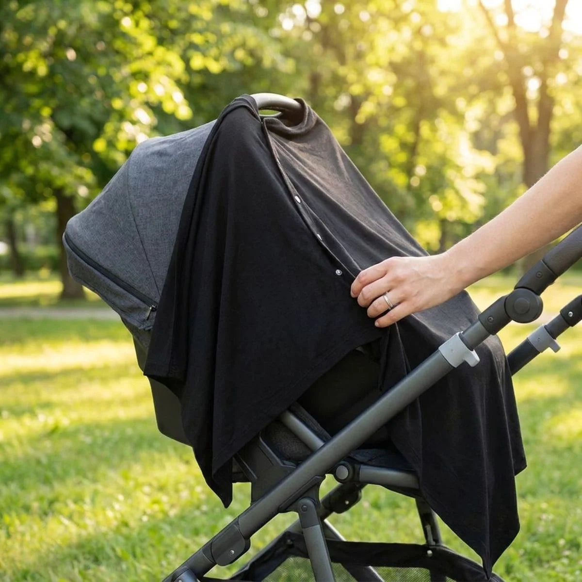 Poncho allaitement Solène™ noir utilisé comme housse de poussette dans un parc verdoyant — usage 3-en-1