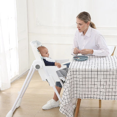 Chaise haute bébé évolutive placée près d’une table à manger, maman nourrit son enfant installé confortablement avec harnais de sécurité.