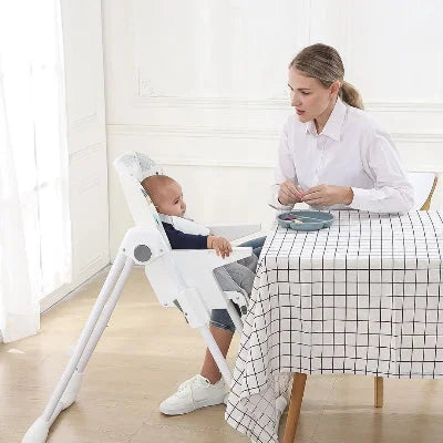 Chaise haute bébé évolutive placée près d’une table à manger, maman nourrit son enfant installé confortablement avec harnais de sécurité.