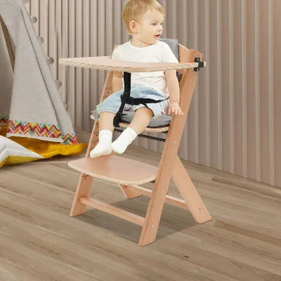 Bébé assis confortablement dans une chaise haute évolutive bois, design naturel avec plateau amovible et harnais sécurisé.