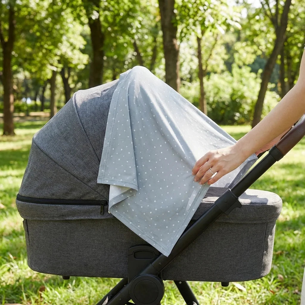 Châle allaitement DouxVoile™ Géo bleu gris étoiles utilisé comme couverture protection poussette dans parc en été — main maman visible