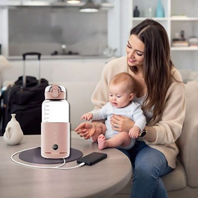 Chauffe biberon rose connecté à un chargeur portable sur une table, utilisé par une mère et son bébé dans un cadre familial chaleureux.