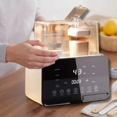 Main d’un parent posée sur le couvercle du chauffe biberon DuoWarm Elite™ en cours de fonctionnement, affichage numérique à 43°C, sur une table en bois avec ustensiles bébé.

