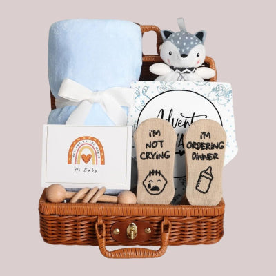 Coffret Naissance Bébé contenant une couverture bleue douce, un doudou renard, des chaussettes humoristiques, un hochet en bois et une carte, idéal pour un cadeau de naissance mixte