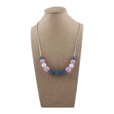 Collier d’allaitement avec perles roses, violettes et blanches en silicone alimentaire, sur support de présentation neutre.
