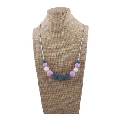 Collier d’allaitement avec perles roses, violettes et blanches en silicone alimentaire, sur support de présentation neutre.