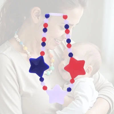 Collier d’allaitement avec perles rouge, bleu et blanc et trois étoiles colorées, porté par une maman souriante en portage, stimulant l’attention et la vue de bébé.

