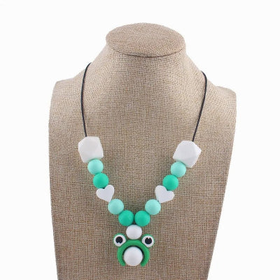 Collier d'allaitement vert avec pendentif grenouille rigolo, perles rondes et cœurs blancs en silicone, parfait pour l’éveil sensoriel de bébé.