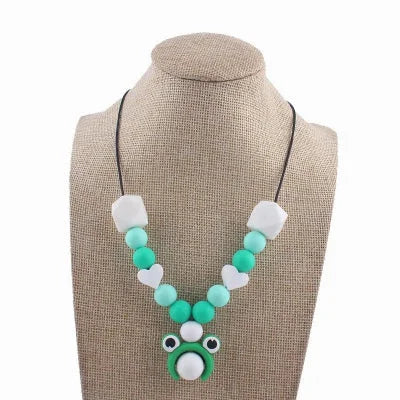 Collier d'allaitement vert avec pendentif grenouille rigolo, perles rondes et cœurs blancs en silicone, parfait pour l’éveil sensoriel de bébé.