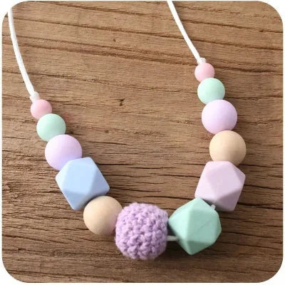 Collier d’allaitement en perles pastel lilas, vert menthe et rose tendre, stimulant la motricité fine de bébé et offrant un soulagement pendant les poussées dentaires.