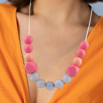 Collier d’allaitement rose et orange porté par une maman, alliant style et utilité pour apaiser bébé et accompagner l’allaitement