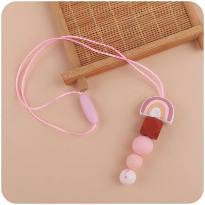 Collier d’allaitement rose pastel à fermoir sécurisé, posé à plat sur fond beige, parfait pour apaiser bébé tout en ajoutant une touche douce et moderne au look de maman.